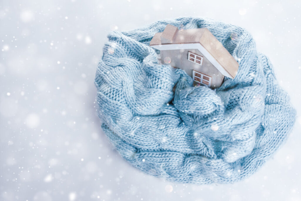 Toy wooden house wrapped in a warm knitted scarf on a white background.