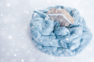 Toy wooden house wrapped in a warm knitted scarf on a white background.